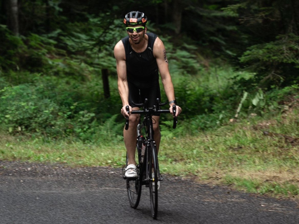 Triathlète tout sourire à vélo sur une route en sous-bois, à Pierre-Percée